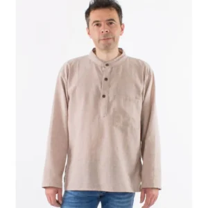 Un homme portant une chemise beige et un jean, se tenant debout avec une expression détendue.